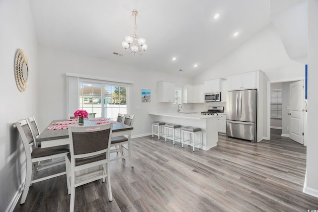 dining room featuring high vaulted ceiling, sink, light hardwood / wood-style flooring, and a notable chandelier