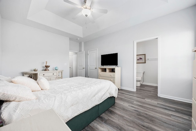 bedroom featuring a raised ceiling, ensuite bathroom, ceiling fan, and dark hardwood / wood-style flooring