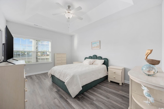 bedroom with a raised ceiling, hardwood / wood-style floors, and ceiling fan