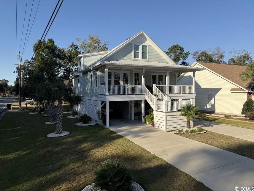 coastal inspired home featuring a front lawn, covered porch, and a carport