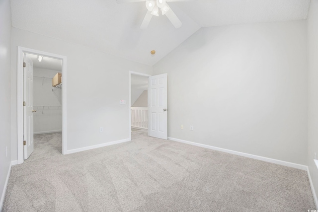 unfurnished bedroom with ceiling fan, light colored carpet, lofted ceiling, a walk in closet, and a closet