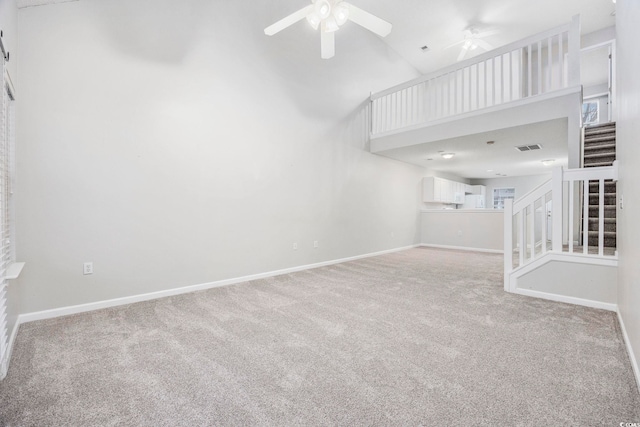 unfurnished living room featuring ceiling fan, light colored carpet, and a towering ceiling