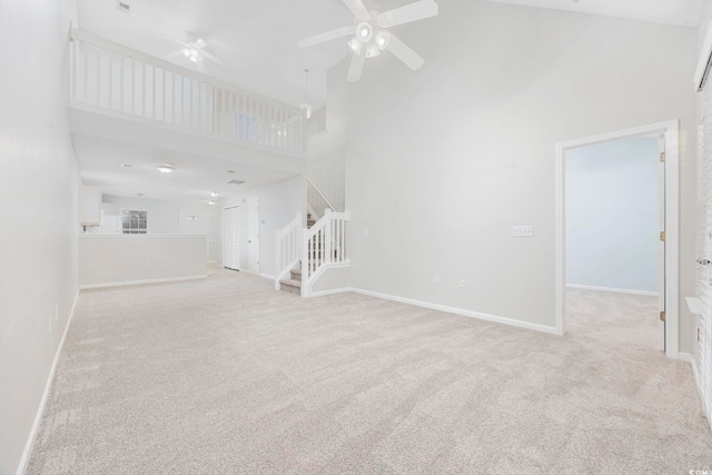 unfurnished living room with ceiling fan, light colored carpet, and a high ceiling