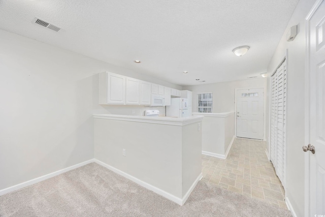 interior space with kitchen peninsula, light carpet, white appliances, a textured ceiling, and white cabinetry