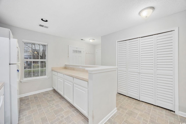 kitchen with white cabinets, a textured ceiling, white refrigerator, and kitchen peninsula