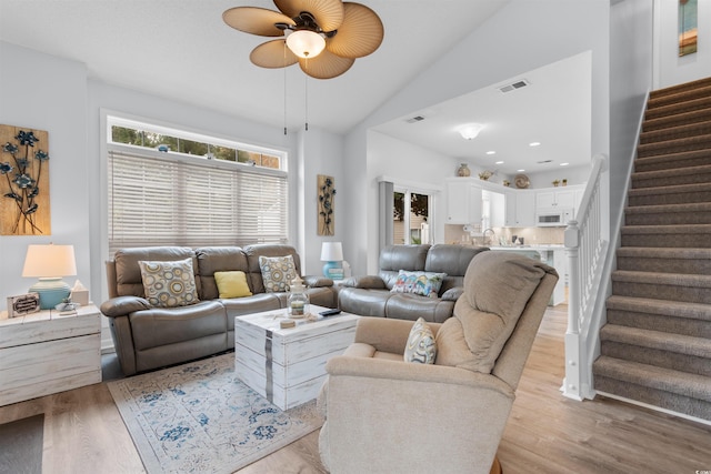 living room featuring ceiling fan, light wood-type flooring, and vaulted ceiling