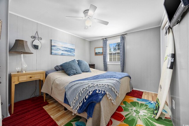 bedroom featuring ceiling fan, crown molding, wood-type flooring, and wooden walls