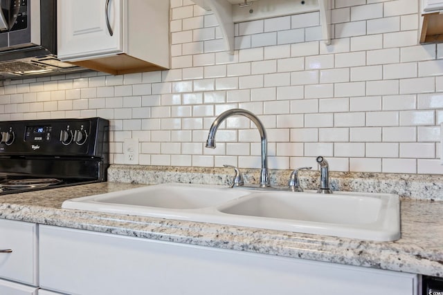 kitchen with white cabinets, black stove, sink, decorative backsplash, and light stone counters