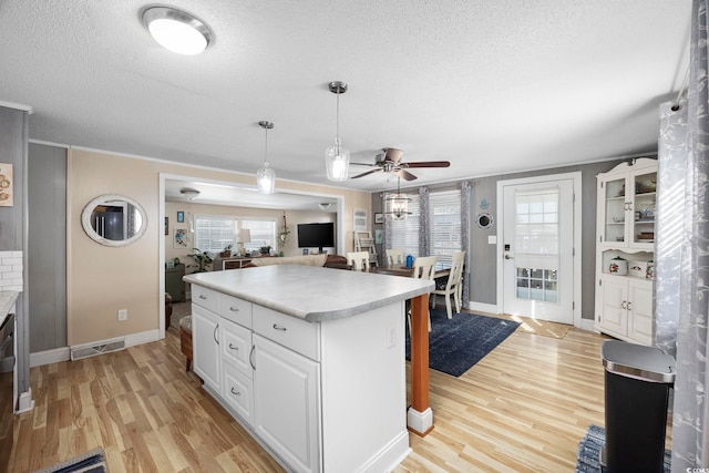 kitchen featuring ceiling fan, light hardwood / wood-style flooring, white cabinets, a kitchen island, and hanging light fixtures