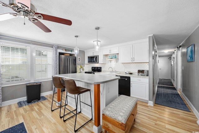 kitchen with black appliances, pendant lighting, light hardwood / wood-style flooring, white cabinets, and a center island