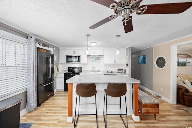 kitchen with white cabinets, pendant lighting, light wood-type flooring, and black appliances