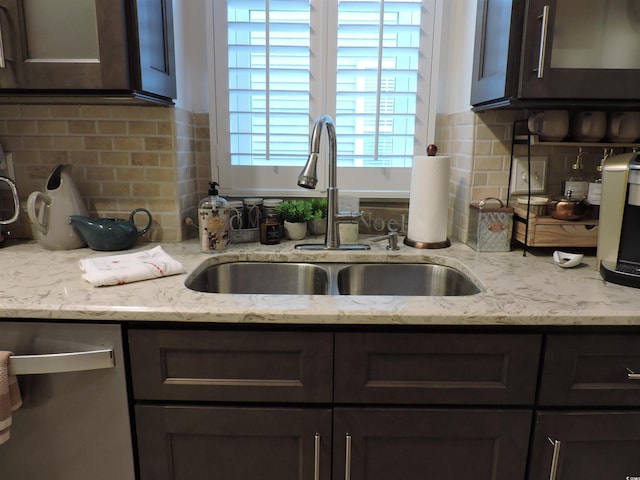 kitchen with light stone countertops, backsplash, dark brown cabinetry, and sink