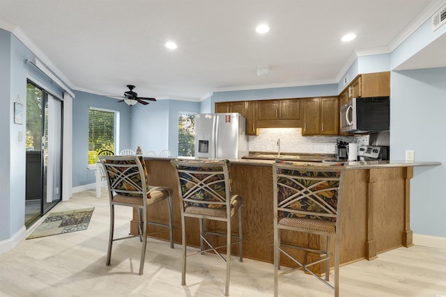 kitchen featuring ornamental molding, appliances with stainless steel finishes, light hardwood / wood-style floors, a kitchen bar, and kitchen peninsula