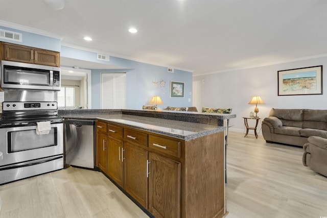 kitchen with light wood-type flooring, stainless steel appliances, crown molding, and a breakfast bar area