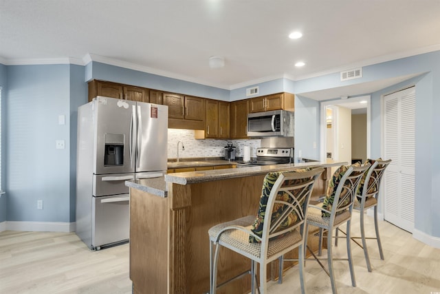 kitchen with appliances with stainless steel finishes, tasteful backsplash, crown molding, sink, and light hardwood / wood-style floors