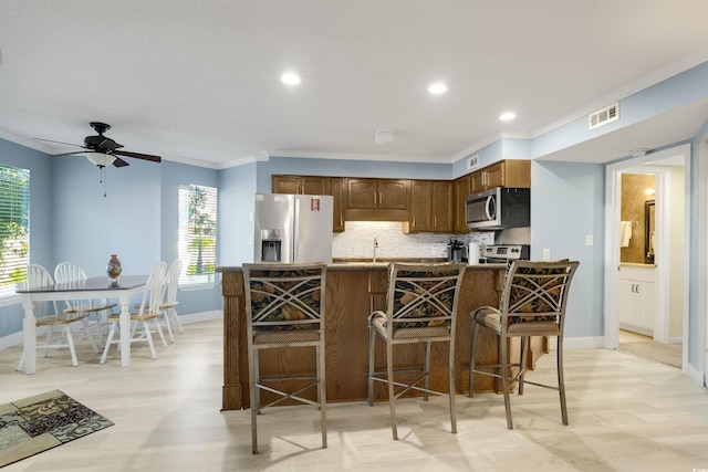 kitchen featuring backsplash, stainless steel appliances, ceiling fan, crown molding, and a breakfast bar area