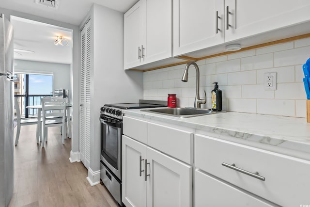 kitchen with light stone countertops, backsplash, sink, white cabinets, and light hardwood / wood-style floors