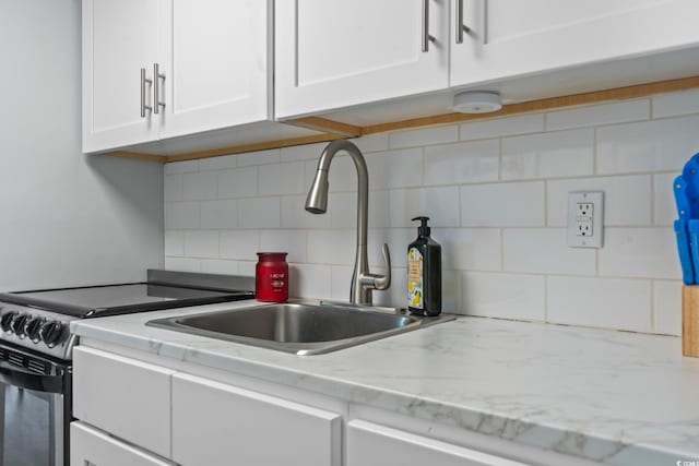 kitchen with light stone countertops, decorative backsplash, electric range oven, sink, and white cabinetry