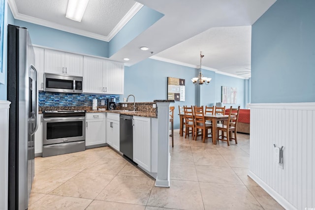 kitchen featuring white cabinetry, hanging light fixtures, kitchen peninsula, crown molding, and appliances with stainless steel finishes