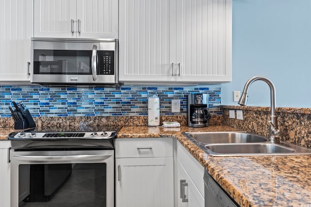 kitchen with sink, tasteful backsplash, dark stone counters, white cabinets, and appliances with stainless steel finishes