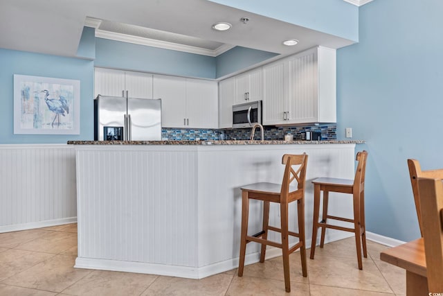 kitchen featuring kitchen peninsula, ornamental molding, stainless steel appliances, dark stone countertops, and white cabinets