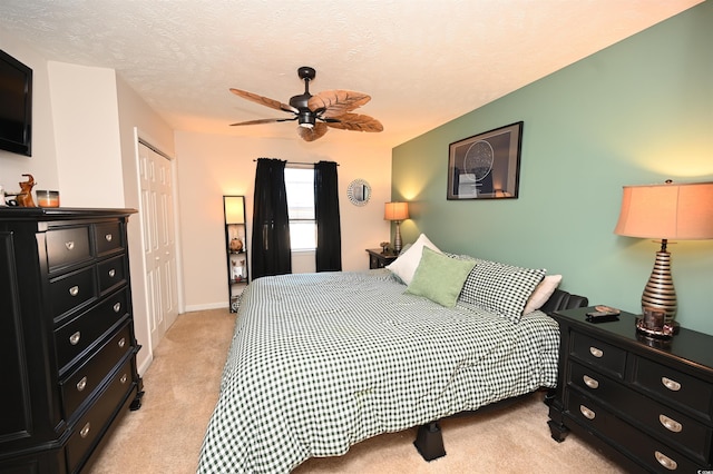 bedroom featuring a textured ceiling, light colored carpet, a closet, and ceiling fan