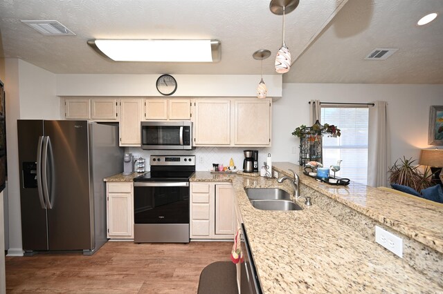 kitchen featuring sink, light hardwood / wood-style flooring, a textured ceiling, decorative light fixtures, and stainless steel appliances