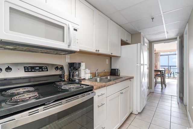 kitchen with a paneled ceiling, white appliances, sink, light tile patterned floors, and white cabinetry