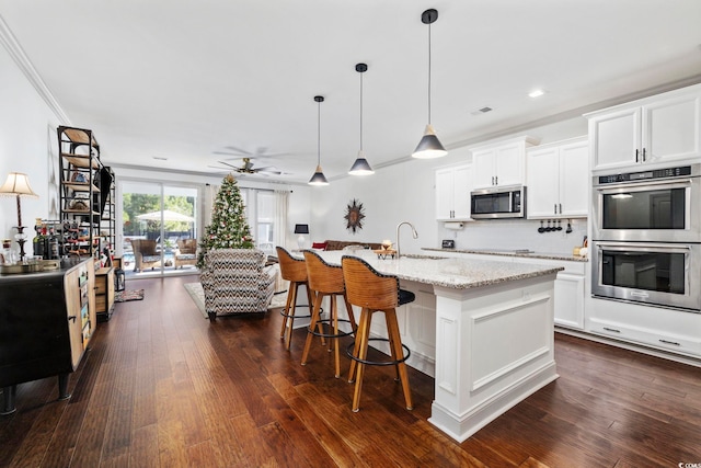 kitchen featuring ceiling fan, dark wood-type flooring, stainless steel appliances, decorative light fixtures, and a center island with sink