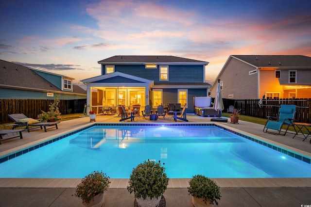 pool at dusk with a sunroom and a patio area