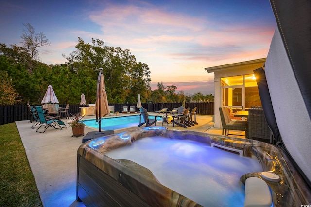 pool at dusk with a patio and a hot tub