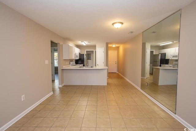 kitchen with stainless steel refrigerator, kitchen peninsula, white cabinets, and light tile patterned flooring