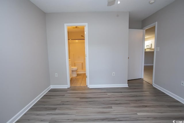 unfurnished bedroom with ensuite bathroom, ceiling fan, and light wood-type flooring