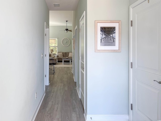 hall featuring baseboards, visible vents, and wood finished floors