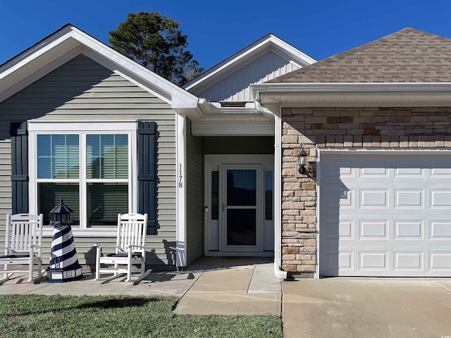 property entrance with board and batten siding, stone siding, a shingled roof, and an attached garage