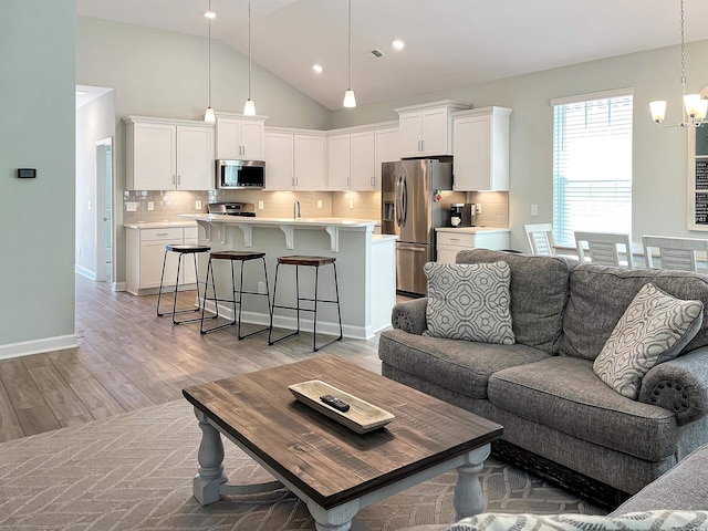 living room with light wood finished floors, baseboards, an inviting chandelier, high vaulted ceiling, and recessed lighting