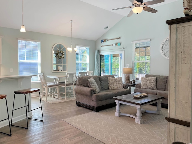 living room with ceiling fan with notable chandelier, high vaulted ceiling, light wood finished floors, and visible vents