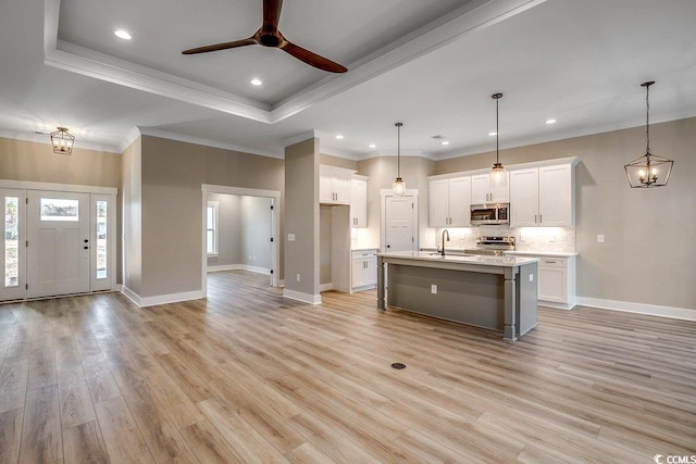 kitchen with light hardwood / wood-style floors, white cabinetry, hanging light fixtures, appliances with stainless steel finishes, and an island with sink