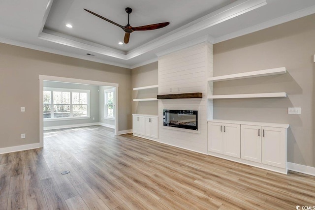 unfurnished living room with a fireplace, light wood-type flooring, ceiling fan, a tray ceiling, and crown molding