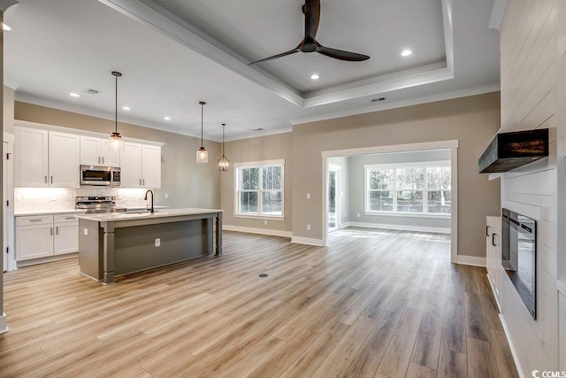 kitchen featuring ceiling fan, hanging light fixtures, an island with sink, stainless steel appliances, and white cabinets