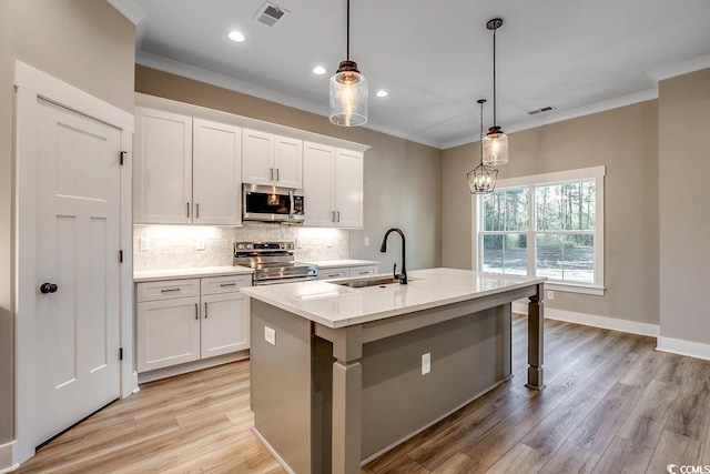 kitchen with hanging light fixtures, white cabinets, stainless steel appliances, and a kitchen island with sink