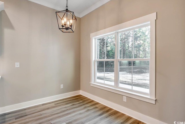 spare room with wood-type flooring, a wealth of natural light, crown molding, and a chandelier