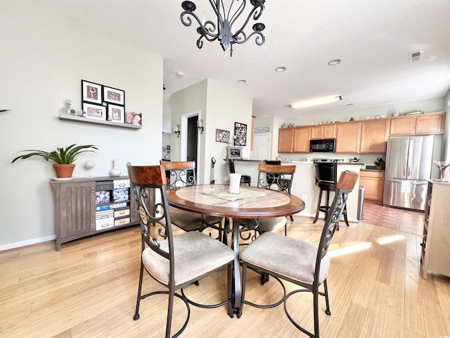 dining area with a textured ceiling, light wood-type flooring, and an inviting chandelier