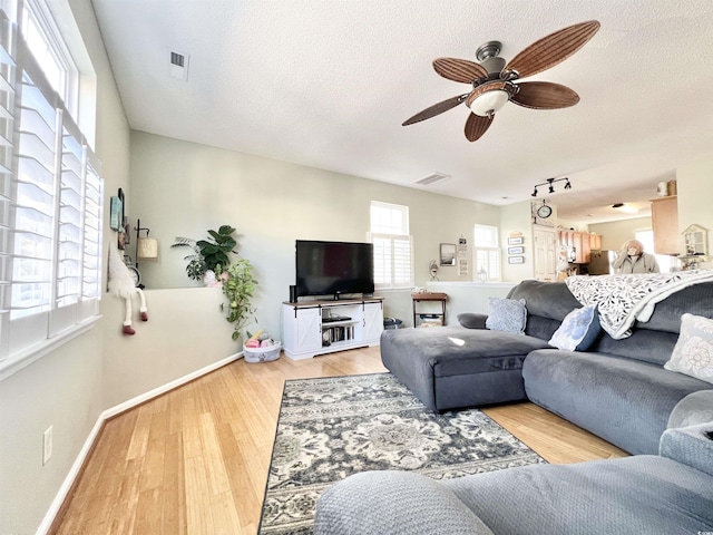 living room with ceiling fan, a textured ceiling, a wealth of natural light, and light hardwood / wood-style flooring