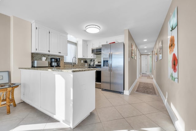 kitchen with kitchen peninsula, decorative backsplash, light stone countertops, stainless steel appliances, and white cabinetry