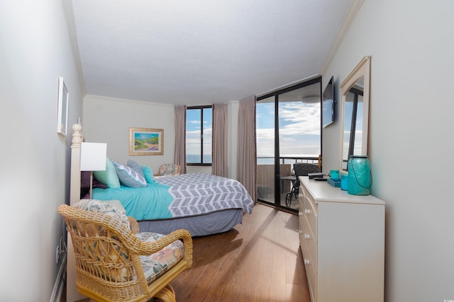 bedroom featuring access to outside, ornamental molding, a textured ceiling, light hardwood / wood-style floors, and a wall of windows