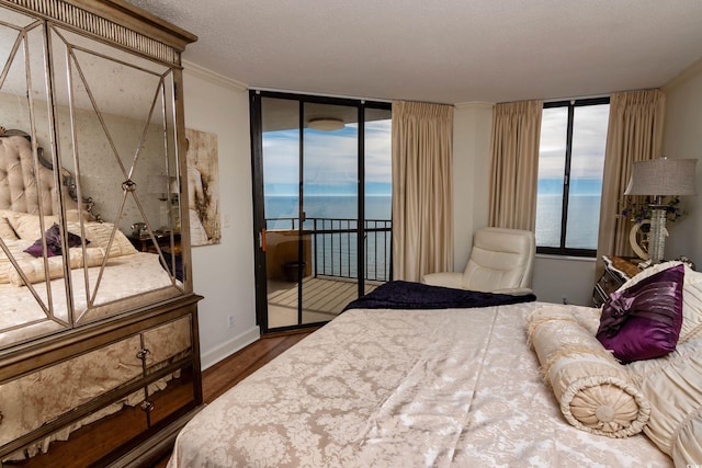 bedroom with access to exterior, a textured ceiling, a water view, and dark wood-type flooring