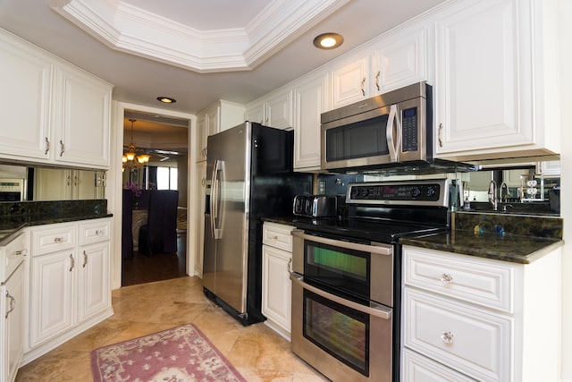 kitchen featuring appliances with stainless steel finishes, dark stone counters, ornamental molding, a raised ceiling, and white cabinets