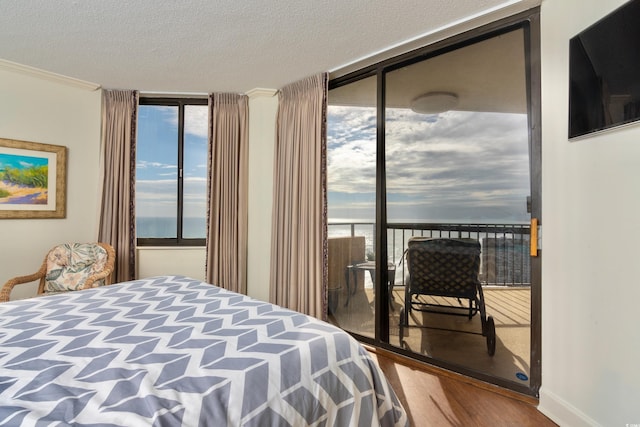 bedroom with ornamental molding, wood-type flooring, a textured ceiling, and a wall of windows