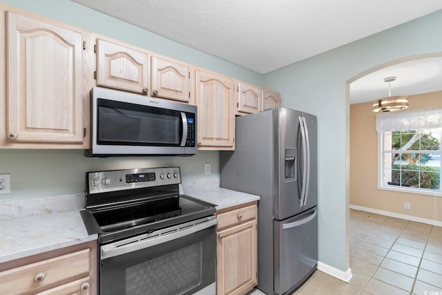 kitchen with light brown cabinets, stainless steel appliances, a notable chandelier, a textured ceiling, and light tile patterned flooring